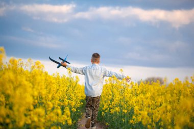 Güneşli bir yaz gününde sarı alanda yürüyen sevimli çocuk. Çocuk kağıt uçak başlatır. Ülkede doğa. Geri görünüm