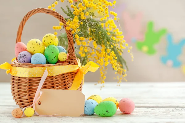 色彩艳丽的复活节彩蛋在一个白色木制背景的篮子里 上面点缀着一丛丛的油菜花 春假概念 — 图库照片