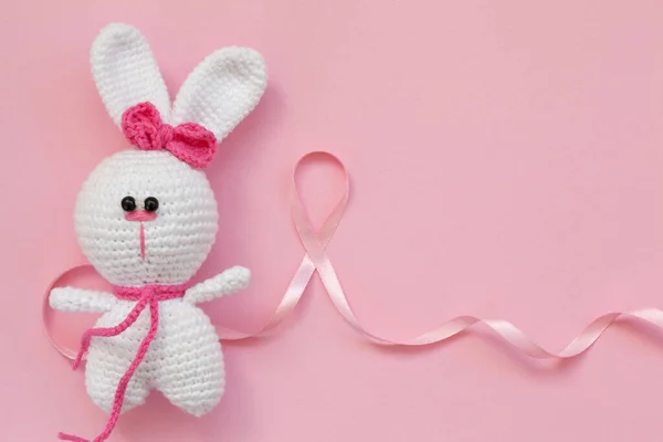 ピンクの背景に小さなニットの赤ちゃんのおもちゃウサギとピンクのリボン乳がん フラットレイアウト トップビュー — ストック写真