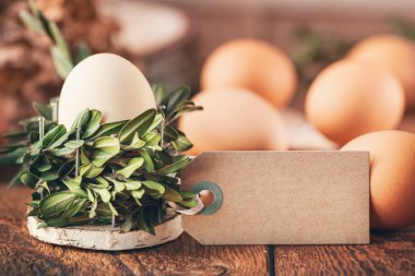 Sepetteki doğal yumurtalar bir demet bitkiden, boş etiketler ise güneşli bir sabahta tahta masadaki yazılar için. Çevre dostu Paskalya konsepti.