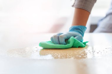 Koruyucu eldivenli bir kadın evini temizlerken masa antibakteriyeli sabun yıkıyor. Virüs önleyici tedbirler için kavram temizliği.