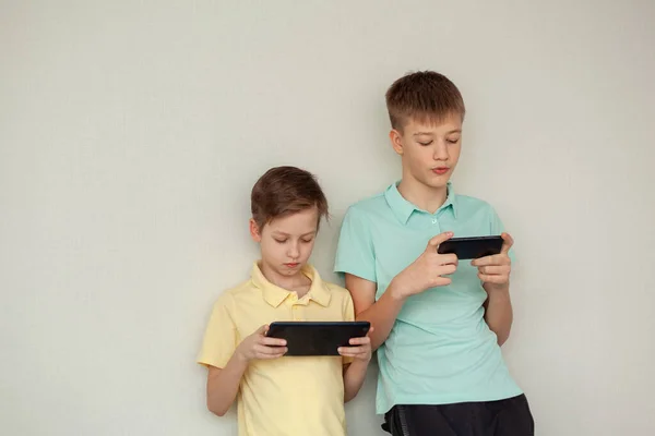 2人の男の子がゲームをしたり 自宅で携帯電話でインターネットで情報ビデオを見ています 遠隔オンライン教育 — ストック写真