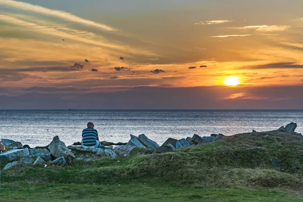 Starší muž na skalnaté pobřeží při západu slunce — Stock fotografie