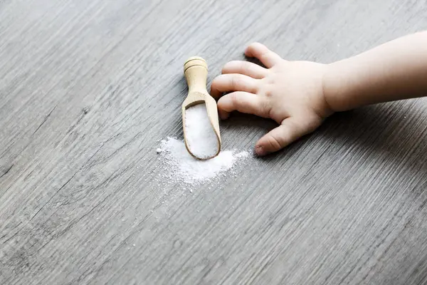 Sal blanca en cuchara de madera sobre la mesa con la mano del niño — Foto de Stock