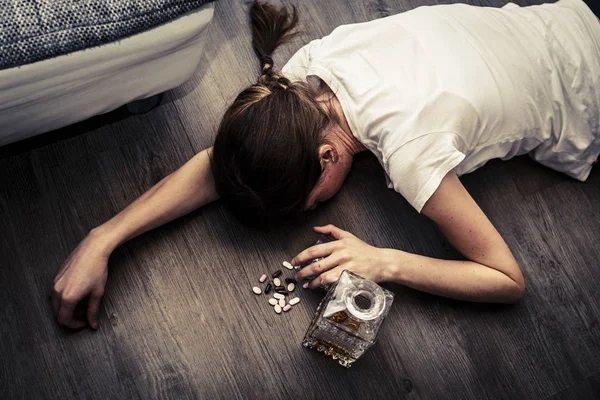 Mujer joven borracha o envenenada con botella de alcohol y pastillas — Foto de Stock