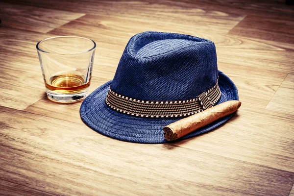 Sombrero azul con cigarro y bebida cara de whisky o ron en el suelo de madera Imagen De Stock