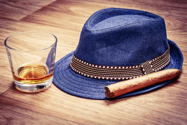 Chapéu azul com charuto e bebida cara de uísque ou rum no chão de madeira — Fotografia de Stock