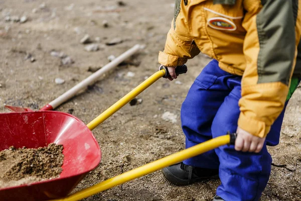 Παιχνίδι του παιδιού με άμμο, κόκκινο φτυάρι και μικρό χαριτωμένο ύψωμα — Φωτογραφία Αρχείου