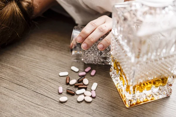 Mujer joven borracha o envenenada con botella de alcohol y pastillas — Foto de Stock