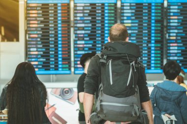 Uçuş bilgi tahtaslarına bakan ve uluslararası havaalanında uçuşlarını kontrol eden yolcular