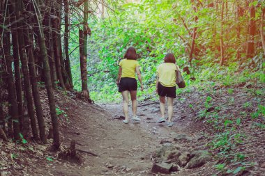 Mutluluğun arka planında aynı kıyafetleri giymiş iki kadın ormanda yürüyüş yolu boyunca yürüyorlar..