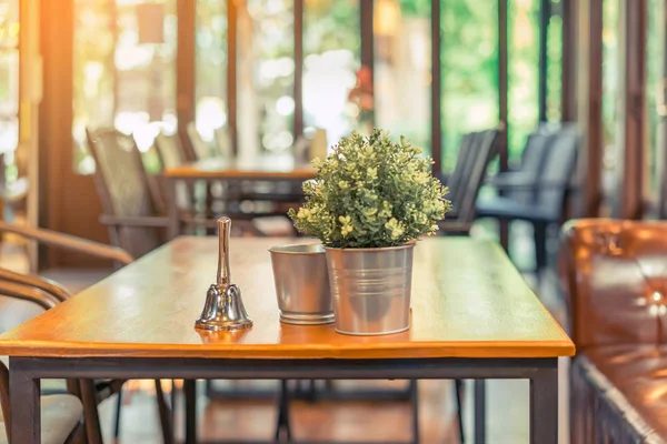 Une petite cloche pour appeler le serveur et des fleurs artificielles dans une casserole en aluminium et une bouteille d'eau potable placée sur une table dans un café. — Photo