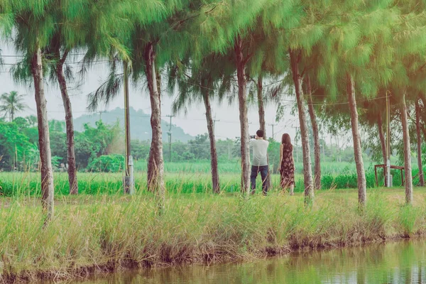 Pareja caminando y tomando fotos bajo los pinos en el parque público. — Foto de Stock