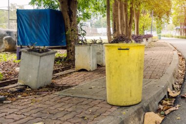 Çevreyi korumak için yürüyüş yolunun yanındaki parkta eski sarı bir çöp tenekesi..