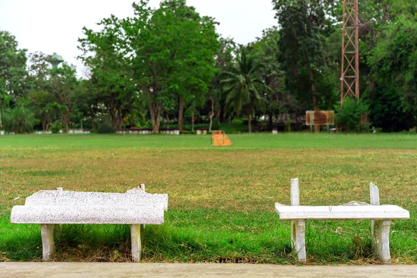 Banco de cimento branco longo velho e quebrado para relaxar após o exercício ao lado do pátio de exercícios no parque público . — Fotografia de Stock