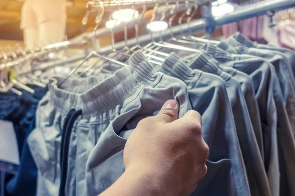 La gente controlla e sceglie pantaloni da acquistare su appendini in un negozio di abbigliamento . — Foto Stock