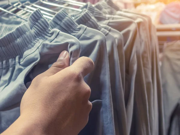 People check and choose pants to buy on hangers in a clothing store.