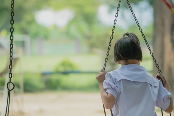 Visão traseira da menina sentar-se no balanço para esperar seu amigo no parque infantil . — Fotografia de Stock