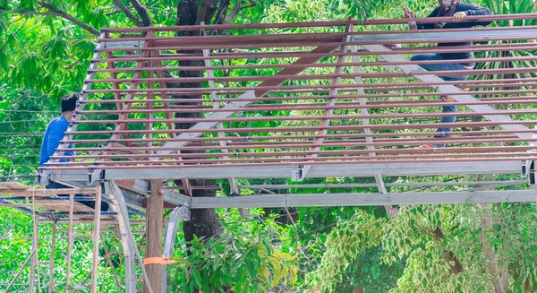 Schweißer und Maler helfen beim Bau einer Giebeldachkonstruktion unter einem großen Mangobaum. — Stockfoto