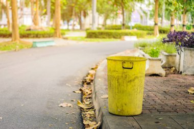 Çevreyi korumak için yürüyüş yolunun yanındaki parkta eski sarı bir çöp tenekesi..