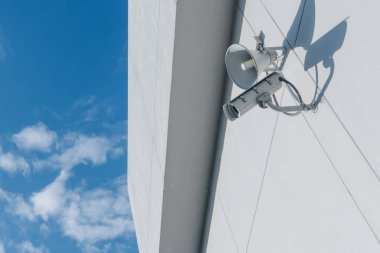 Hoparlörler ve güvenlik kameraları bir binanın duvarında gözlem yapıyor.