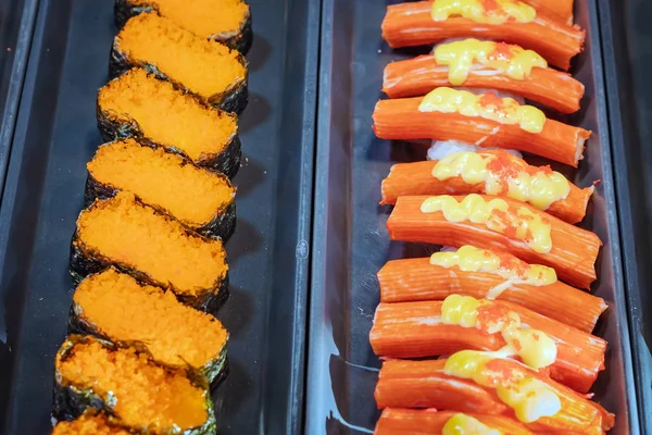 Filas de comida japonesa de sushi. Rollos de Maki ands con atún, salmón, camarones, cangrejo y aguacate. Vista superior de sushi surtido en contenedor de plástico negro que se vende en el mercado. Enfoque selectivo . — Foto de Stock