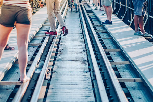 Tourists walk across across rail train tracks from side to another side while visiting The Bridge Over the River Kwai in Kanchanaburi, Thailand.