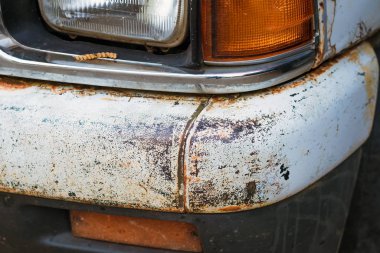Eski beyaz bir kamyonun ön tamponunda çürümeye ve paslanmaya kadar git. Eski, yıpranmış metal yüzeydeki pas deliği..