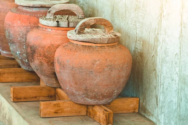 Fila de tarros de barro con tapas de madera y suelo gris áspero para el almacenamiento de agua en la casa asiática. Enfoque selectivo en tapas de madera . — Foto de Stock