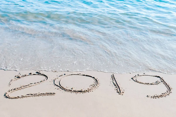 End of  2019 handwritten on the sandy beach with ocean wave washing away with water.. Happy new year 2020 concept.