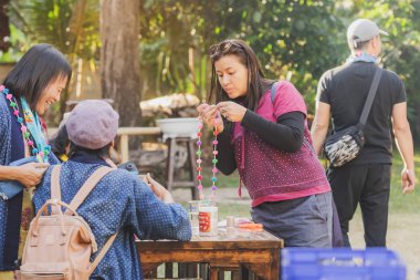 Tanımlanamayan Tayland 'lı kadın turistler, Tayland' ın Lamphun kentindeki Karen köyünde 12 Aralık 2019 tarihli iplik balosundan kolye yapmayı öğreniyor.
