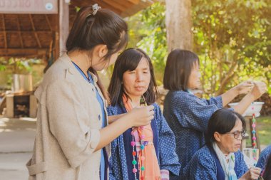Tanımlanamayan Tayland 'lı kadın turistler, Tayland' ın Lamphun kentindeki Karen köyünde 12 Aralık 2019 tarihli iplik balosundan kolye yapmayı öğreniyor.