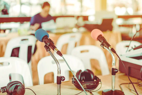 Two microphones with blue and red sponges placed on a stand with earphones on the table with blur image of the audio technician was installing and testing the sound system in the background.