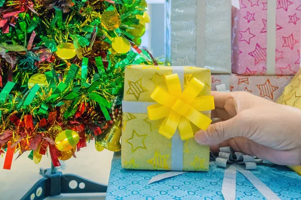 Женская рука берет красиво украшенную подарочную коробку из большой пачки подарков возле елки . — стоковое фото