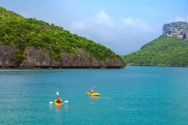 ANG THONG MARINE PARK, SAMUI, TAILANDIA - 13 DE OCTUBRE DE 2019: Turistas navegando en kayak en azul Océano turquesa idílico para explorar cerca de la isla con exuberantes árboles de selva verde y montañas de piedra caliza en el Parque Nacional Marino Ang Thong, Tailandia . — Foto de Stock