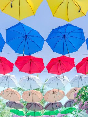 Gökyüzünün üst tarafında asılı renkli şemsiyelerle süslenmiş bir cadde. Renkli şemsiyeler.