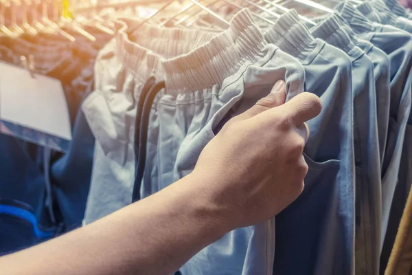 People check and choose pants to buy on hangers in a clothing store.