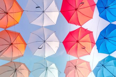 Gökyüzünün üst tarafında asılı renkli şemsiyelerle süslenmiş bir cadde. Renkli şemsiyeler.