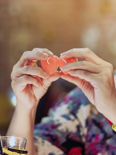 Een rode hartvormige kaars in de hand van een vrouw met kaarslicht in vele kleine glazen bekertjes. Een Valentijnsdag achtergrond. — Stockfoto