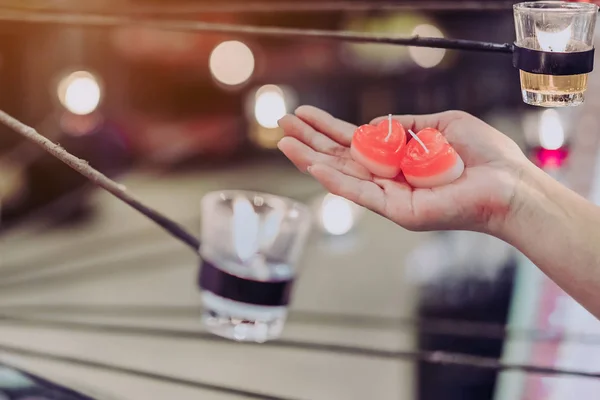 Een rode hartvormige kaars in de hand van een vrouw met kaarslicht in vele kleine glazen bekertjes. Een Valentijnsdag achtergrond. — Stockfoto