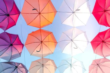 Gökyüzünün üst tarafında asılı renkli şemsiyelerle süslenmiş bir cadde. Renkli şemsiyeler.