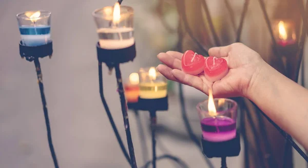 Красная свеча в форме сердца в руке женщины со свечой во многих маленьких стеклянных чашках. День святого Валентина фон . — стоковое фото