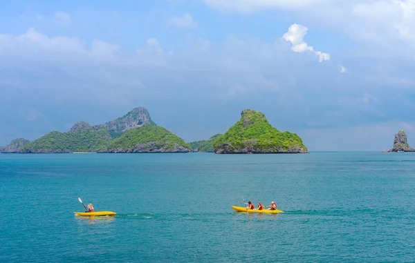 ANG THONG MARINE PARK, SAMUI, TAILANDIA - 13 DE OCTUBRE DE 2019: Turistas navegando en kayak en azul Océano turquesa idílico para explorar cerca de la isla con exuberantes árboles de selva verde y montañas de piedra caliza en el Parque Nacional Marino Ang Thong, Tailandia . — Foto de Stock