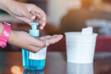 Genç bir kadın elini dezenfektan şişesine bastırıp elini temizliyor. El dezenfektanı alkollü jel, temiz elleri ovuşturur. Koronavirüs salgınını önler. Grip virüsü kavramları, Covid-19 (Coronavirus hastalığı).