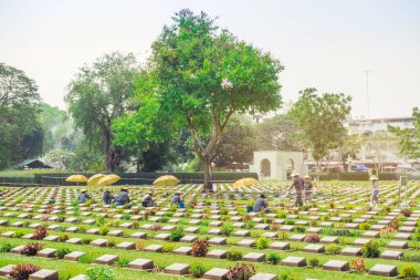 KANCHANABURI THAILAND - 21 Şubat: Kimliği belirsiz işçiler, 21 Şubat 2020 'de Kanchanaburi, Tayland' daki Kanchanaburi Müttefik Savaş Mezarlığı 'nda çiçek yenileyip dekore ediyorlar