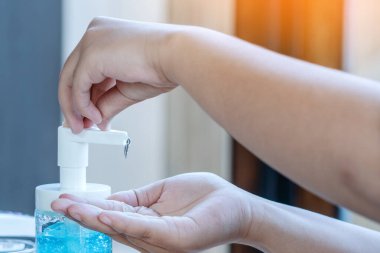 Genç bir kadın elini dezenfektan şişesine bastırıp elini temizliyor. El dezenfektanı alkollü jel, temiz elleri ovuşturur. Koronavirüs salgınını önler. Grip virüsü kavramları, Covid-19 (Coronavirus hastalığı).