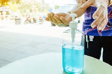 Adam elini şehrin öbür ucunda elini temizlemek için dezenfektan şişesine bastırıyor. Grip virüsü, Covid-19 (Coronavirus hastalığı). Alkol jeli şişesine odaklan.