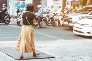 Asyalı bir kadının arka görüntüsü şehir merkezinde yaya geçidinde yürürken telefonu kullanıyor..