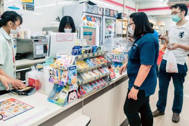 KANCHANABURI, THAILAND - 27 Mart 2020 'de Kanchanaburi, Tayland' da 27 Mart 2020 'de mikropların yayılmasını önlemek için tanımlanamayan kasiyer veya 7-11 personel ve tıbbi koruyucu maskeli müşteriler.