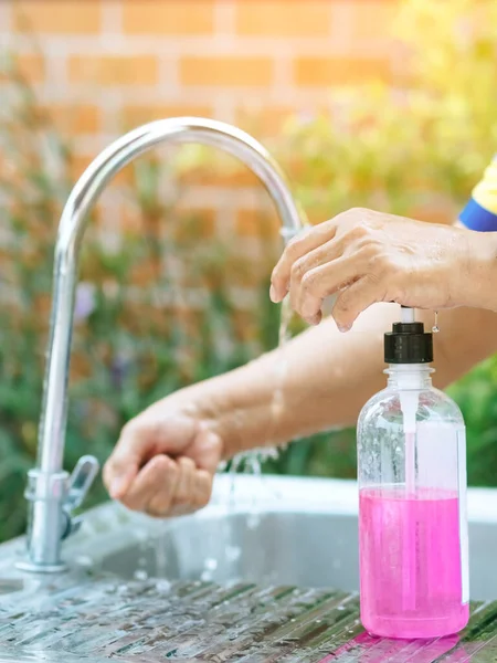A woman washing hands from the tap with pink soap in a aluminium tub. Concepts of Flu virus, Covid-19 (Coronavirus disease). Selective focus.